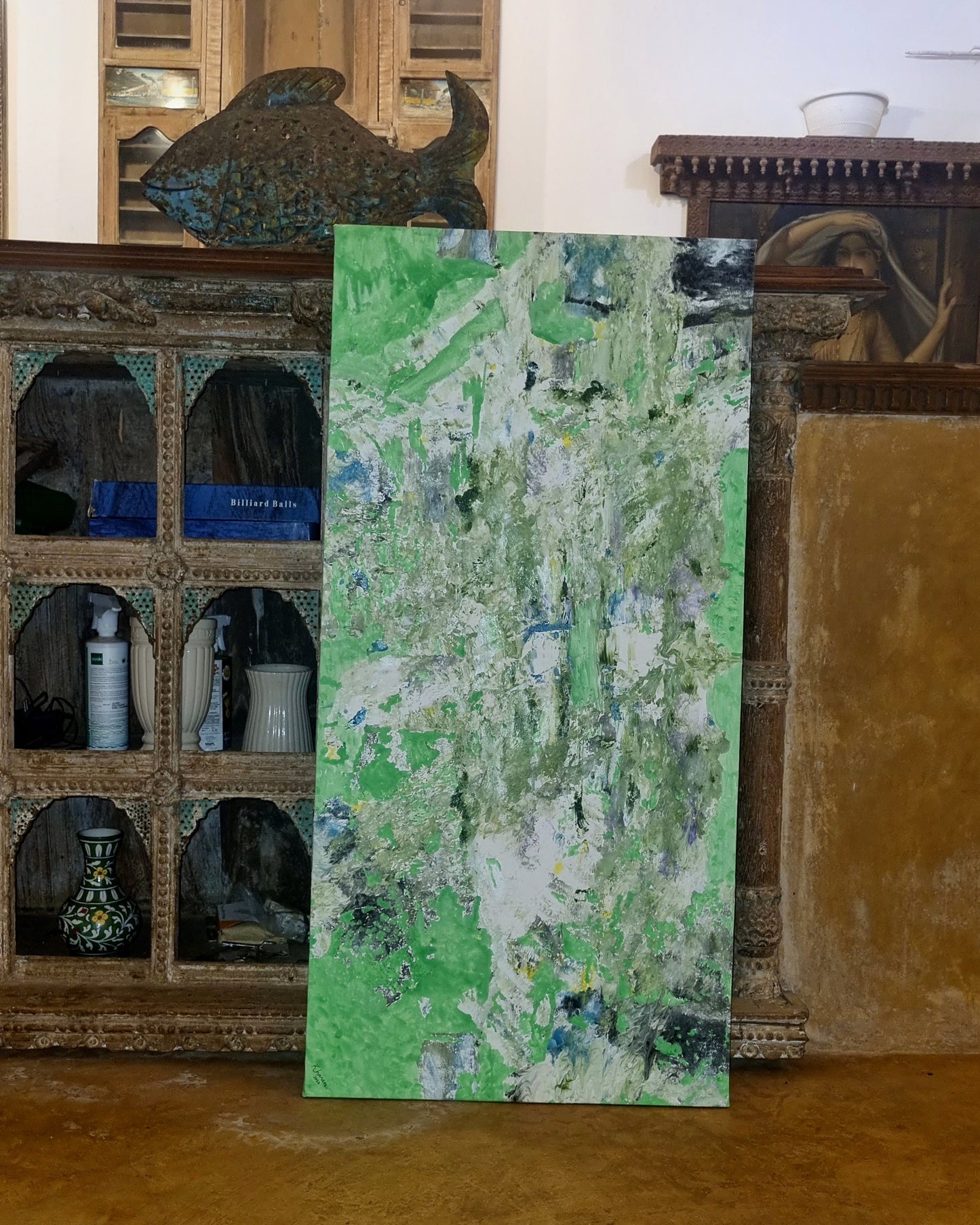 Green abstract painting leaning against a rustic wooden wall with shelves.