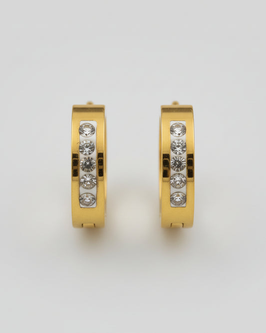 Gold hoop earring with embedded stones on a textured surface