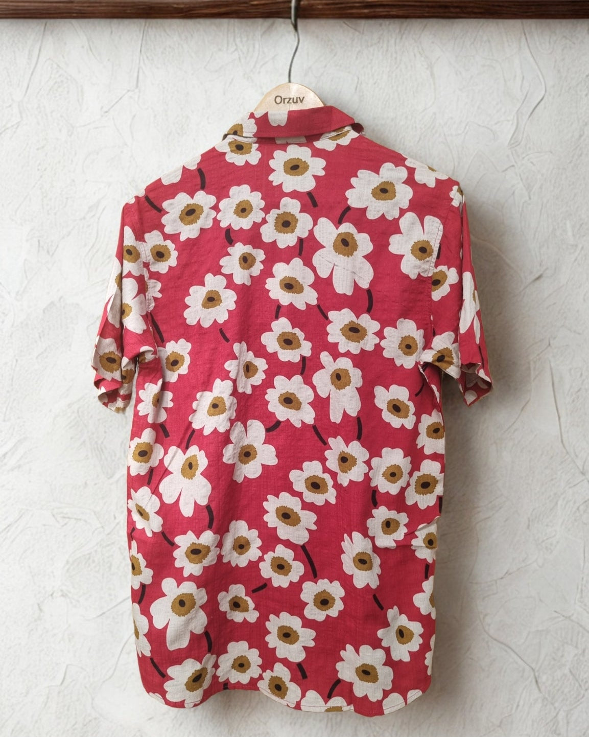 Red floral shirt on a hanger against a textured white wall with 'CHI' branding.