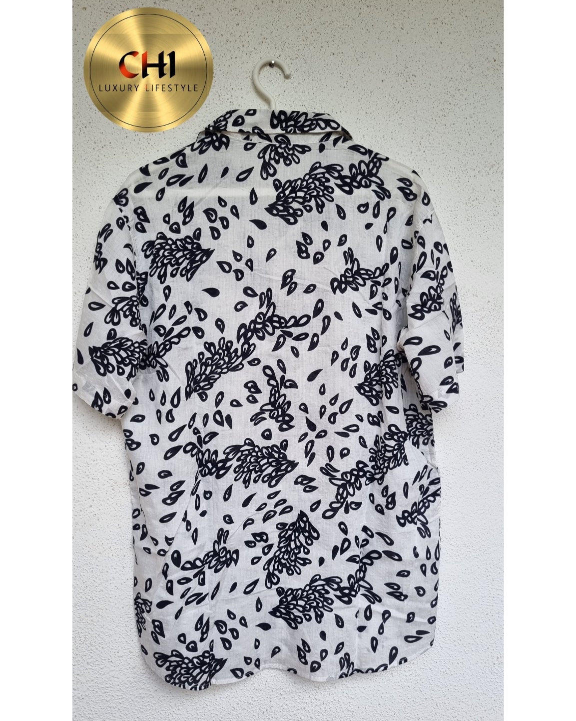 White blouse with black floral pattern on a hanger against a light gray background, with 'CHI' brand logo.