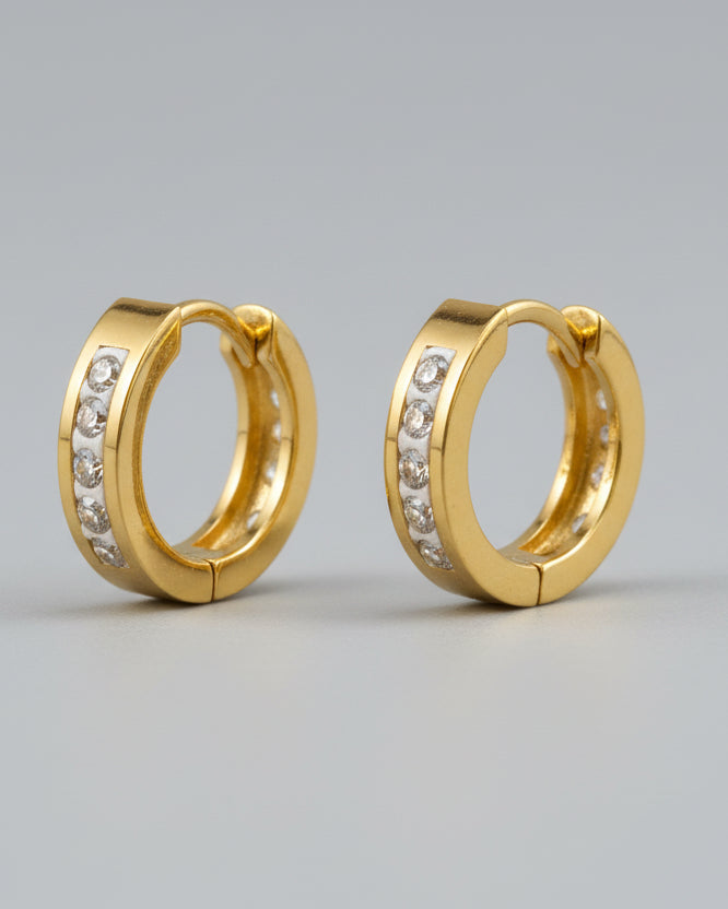 Gold hoop earrings with embedded stones on a textured surface