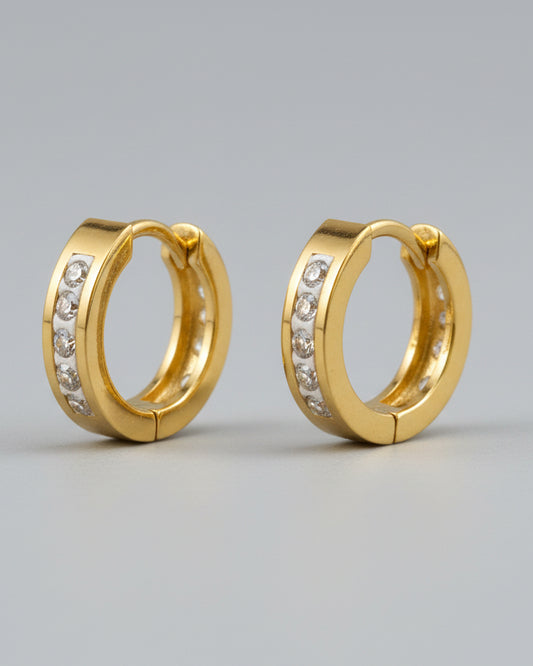 Gold hoop earrings with embedded stones on a textured surface