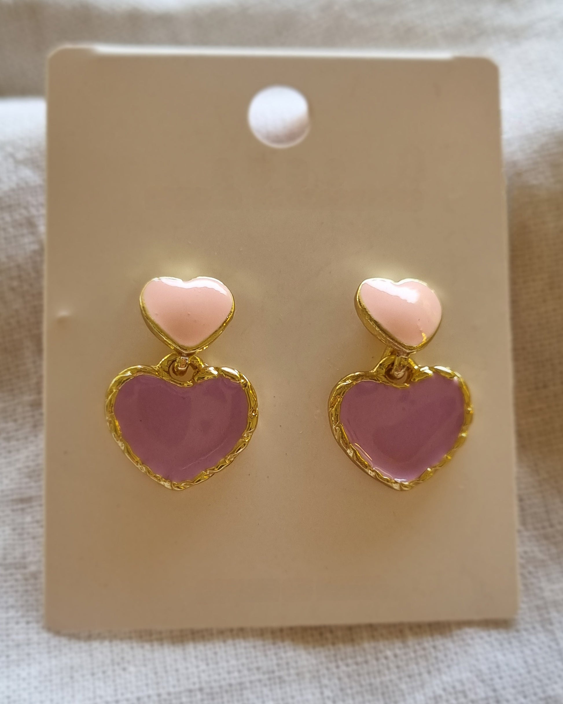 Heart-shaped earrings on a beige card with a textured background