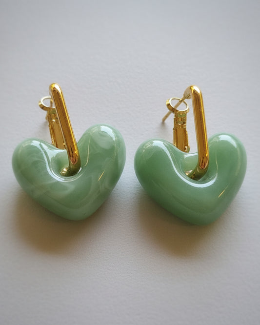 Green heart-shaped earrings with gold hooks on a textured fabric background
