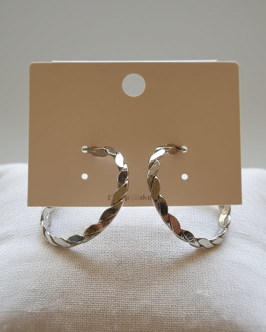 Silver hoop earrings on a beige card with a textured beige background