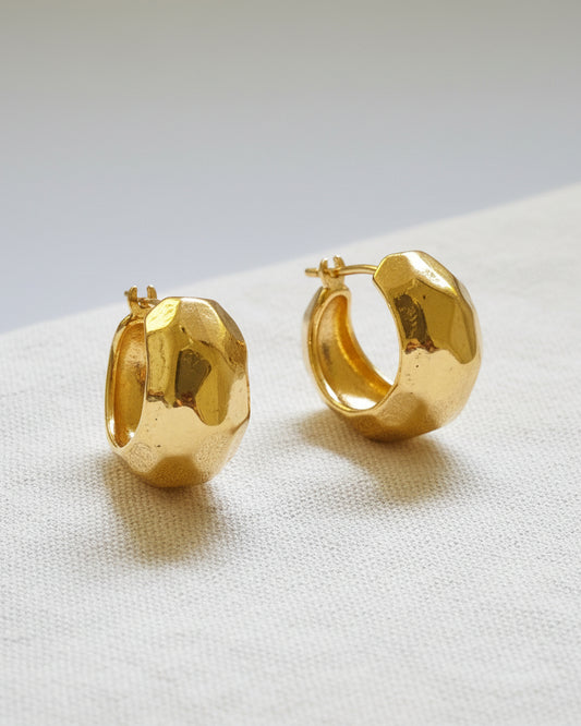 Pair of gold hoop earrings on a textured beige surface