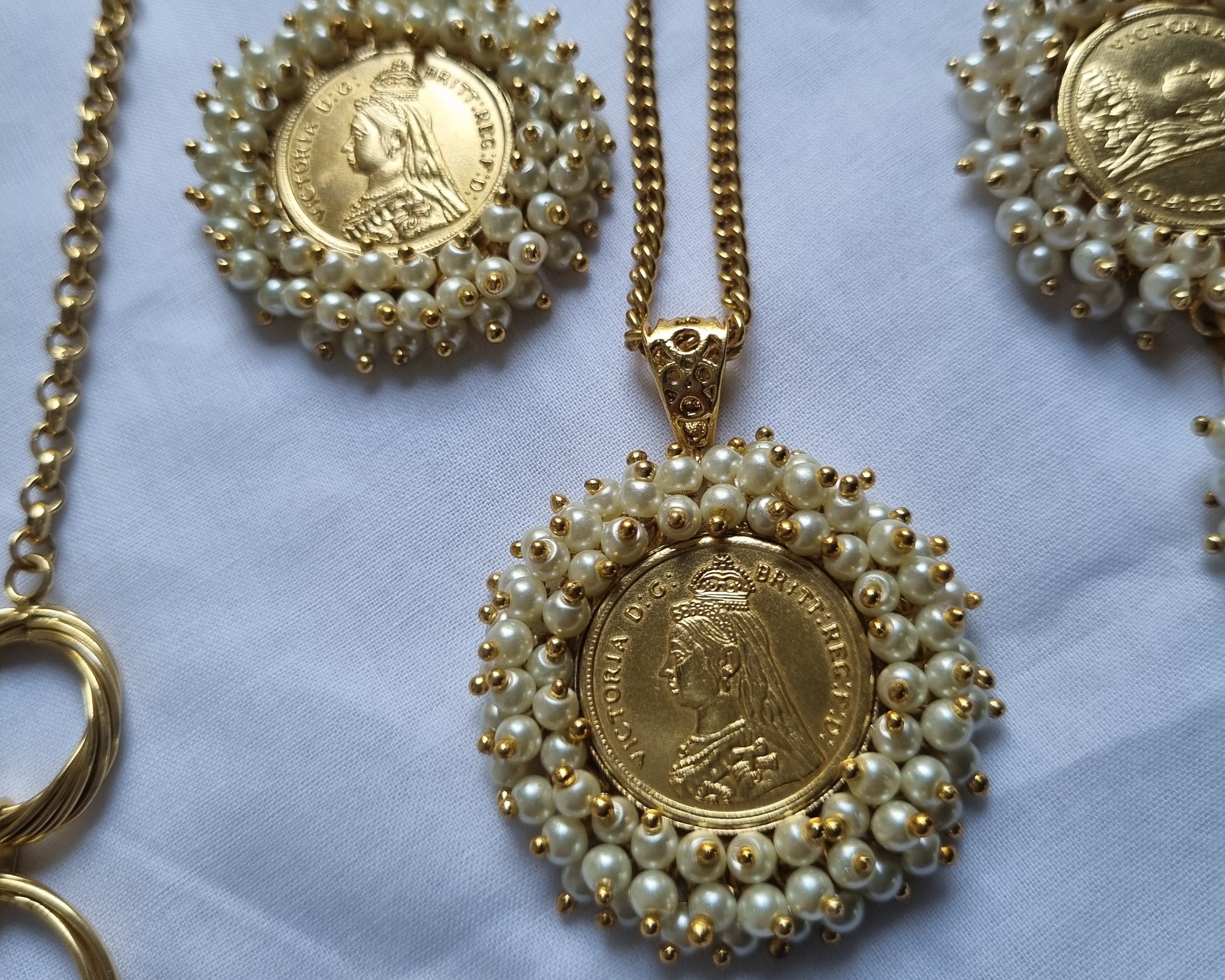 Gold necklaces with coin and pearl designs on a white fabric background