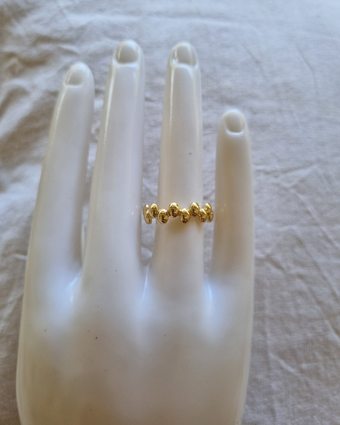 Gold ring on a mannequin hand against a textured white background